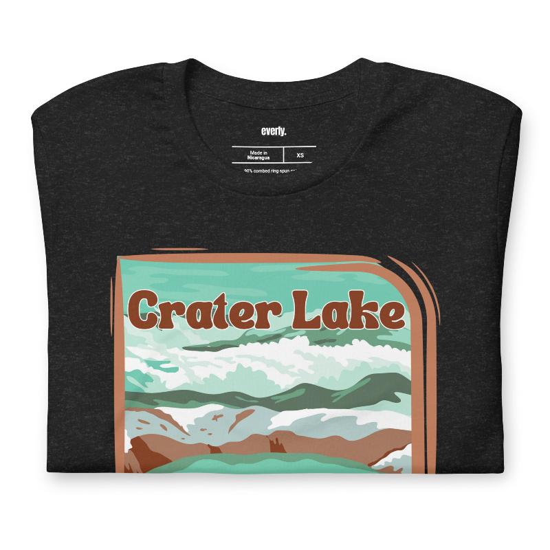 a colorful graphic of Crater Lake National Park, featuring mountains, water, and the text "Crater Lake National Park Oregon 1902 on a black shirt. 