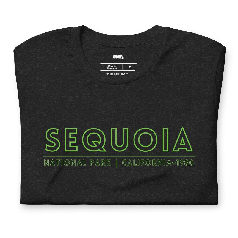 a colorful, detailed graphic of Sequoia National Park with the park's name and established year on the back, and a simplified text logo on the front on a black shirt.