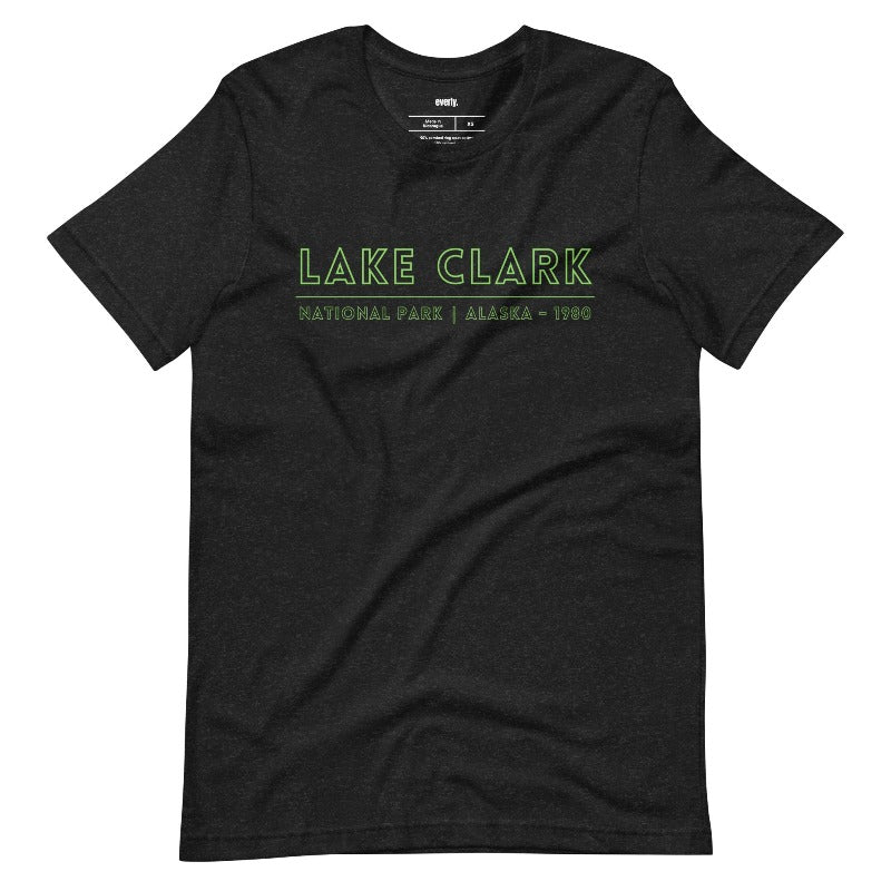 Back view of a black heather Bella + Canvas 3001 unisex shirt featuring a colorful design of Lake Clark National Park with mountains, lake, and wildlife. Inset shows the front view with "Lake Clark National Park | Alaska - 1980" text on a black shirt