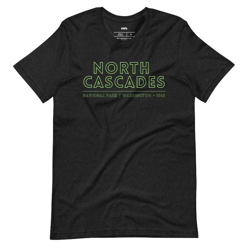 a vibrant, retro-style design of North Cascades National Park on the back, and "North Cascades National Park | Washington - 1968" text on the front on a black shirt.