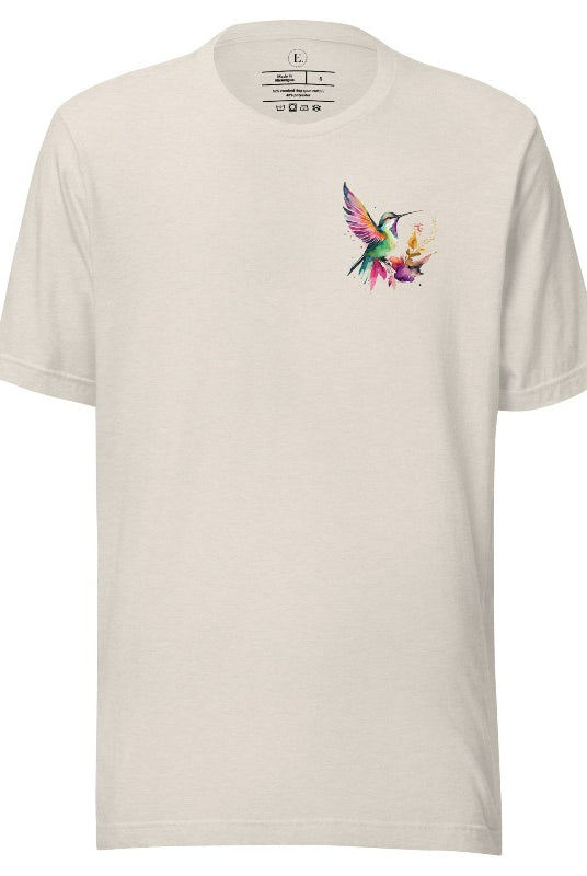 Elevate your style with our stunning t-shirt featuring a watercolor hummingbird delicately placed on the pocket on a heather dust shirt. 