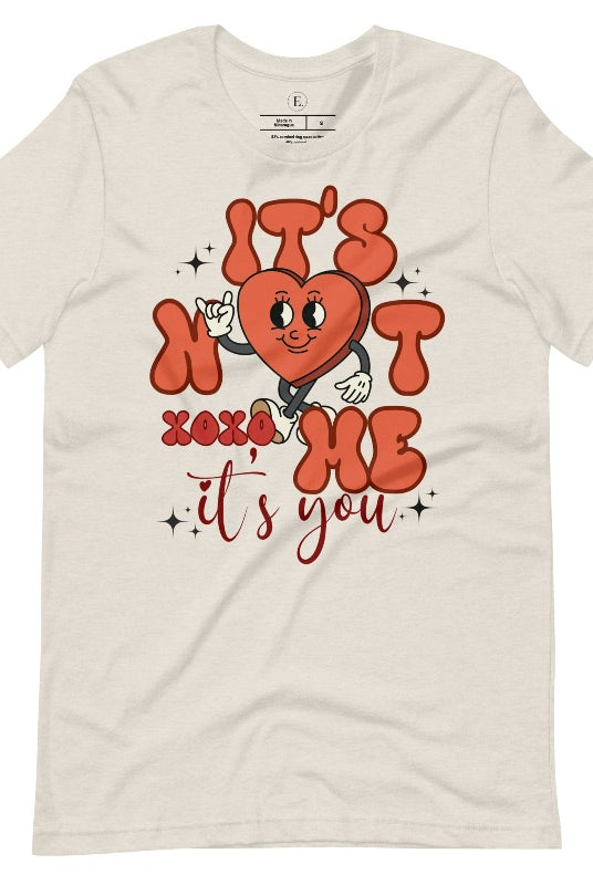 Celebrate Valentine's with our playful shirt! Featuring a bold heart and the message "It's not me, it's you," on a heather dust colored shirt. 