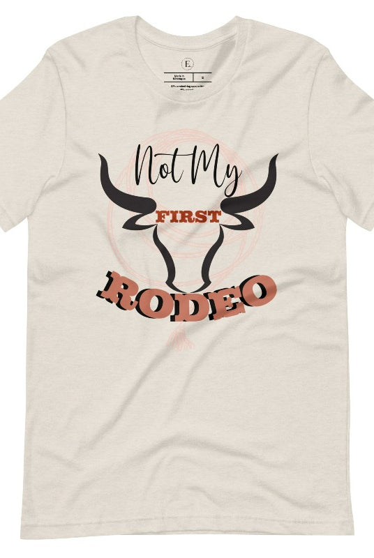 Unleash your cowboy spirit with our country western t-shirt boasting the statement "Not my First Rodeo" alongside bold bull horns and a lasso design on a heather dust colored shirt. 