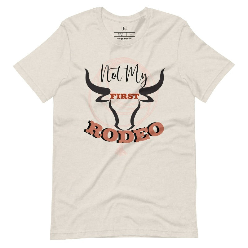 Unleash your cowboy spirit with our country western t-shirt boasting the statement "Not my First Rodeo" alongside bold bull horns and a lasso design on a heather dust colored shirt. 