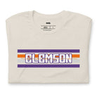 Bella + Canvas 3001 unisex shirt with Clemson University stripe design in purple, orange, and white, with "Clemson" written in bold letters on a beige graphic tee.