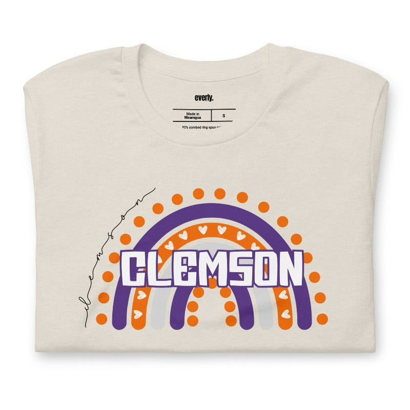 Bella + Canvas 3001 unisex shirt featuring a colorful rainbow design with the word "Clemson" in the center, representing Clemson University on a beige graphic tee.