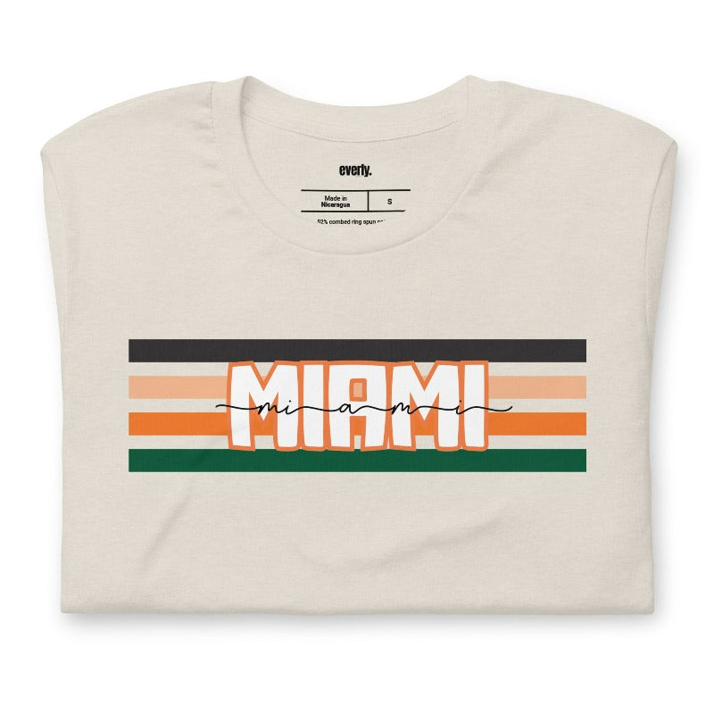 Bella + Canvas 3001 unisex t-shirt featuring the University of Miami design with black, orange, and green stripes and "Miami" text in the center on a beige shirt.