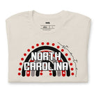 This vibrant NC State design with "North Carolina" text, rainbow arch, and red dots on a beige shirt.