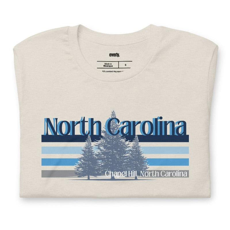 Serene Chapel Hill pine tree design with "North Carolina" and blue and white stripes on a beige graphic tee.