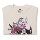 A Halloween-themed design with a skull adorned with flowers and a raven, accompanied by the text "Be Original." The shirt is soft and perfect for celebrating Halloween in style on a beige shirt.