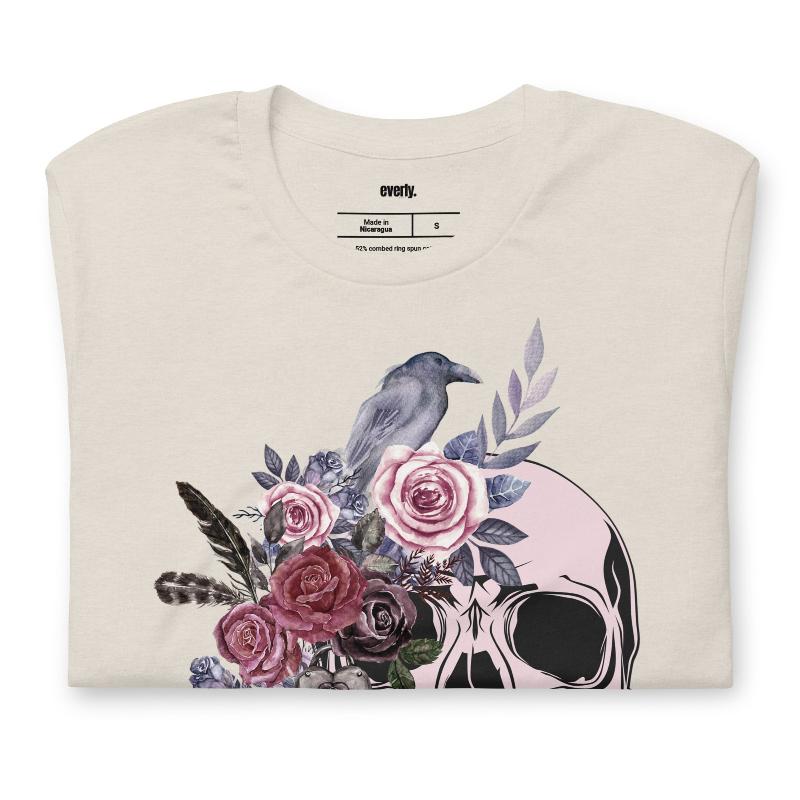 A Halloween-themed design with a skull adorned with flowers and a raven, accompanied by the text "Be Original." The shirt is soft and perfect for celebrating Halloween in style on a beige shirt.