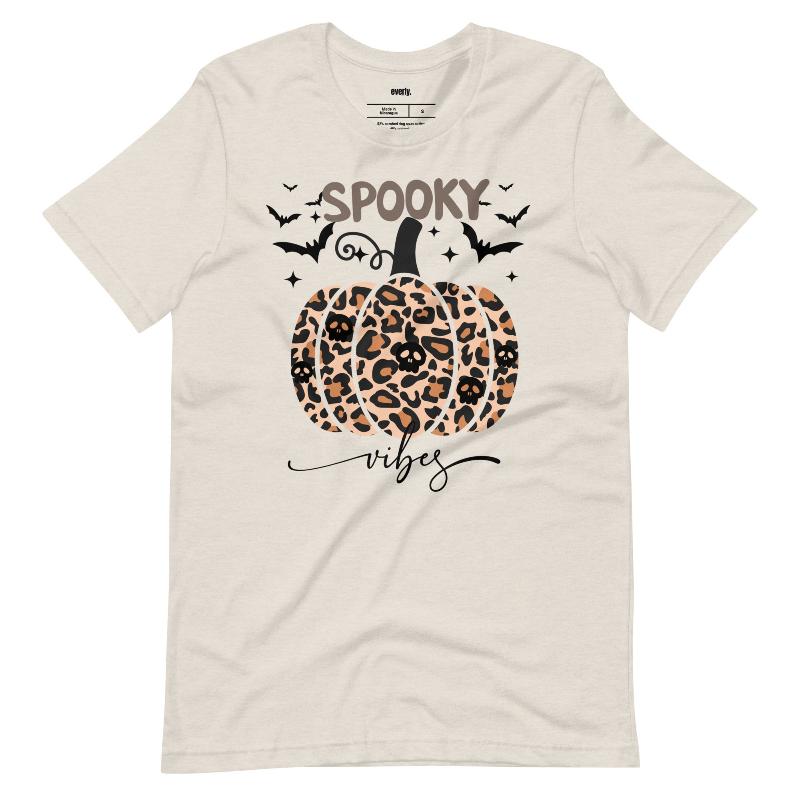 Beige t-shirt featuring a leopard-print pumpkin and "Spooky Vibes" text surrounded by bats, perfect for Halloween and fall season style.