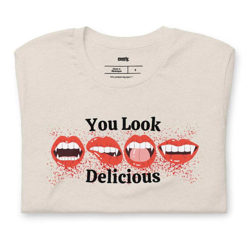 Beige t-shirt featuring a graphic of fanged red lips with the playful phrase "You Look Delicious" splattered in red, perfect for Halloween.