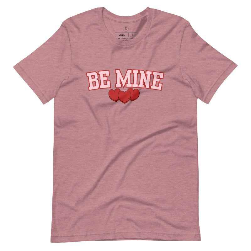Elevate your Valentine's Day style with our "Be Mine" shirt! Featuring bold athletic lettering and three adorable hearts, on a heather orchid colored shirt. 