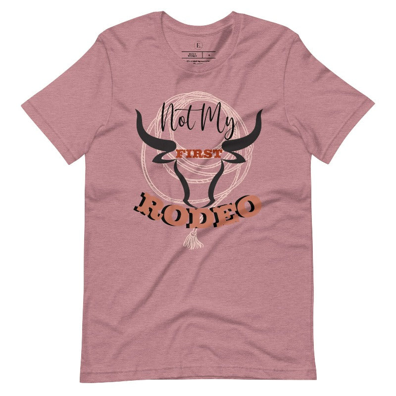 Unleash your cowboy spirit with our country western t-shirt boasting the statement "Not my First Rodeo" alongside bold bull horns and a lasso design on a heather orchid colored shirt. 
