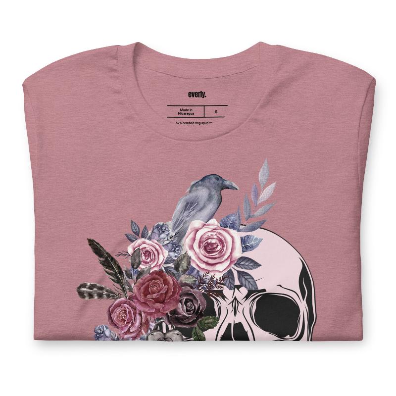 A Halloween-themed design with a skull adorned with flowers and a raven, accompanied by the text "Be Original." The shirt is soft and perfect for celebrating Halloween in style on a muave shirt.