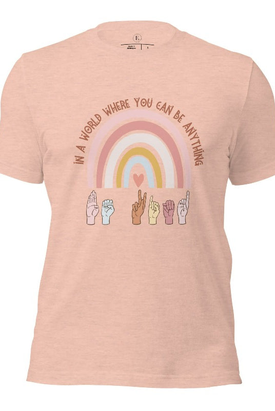 American sign language shirt with a rainbow and the phrase "In a world where you can be anything" and hands signing 'Be Kind' at the bottom on the rainbow on a heather prism peach colored shirt.