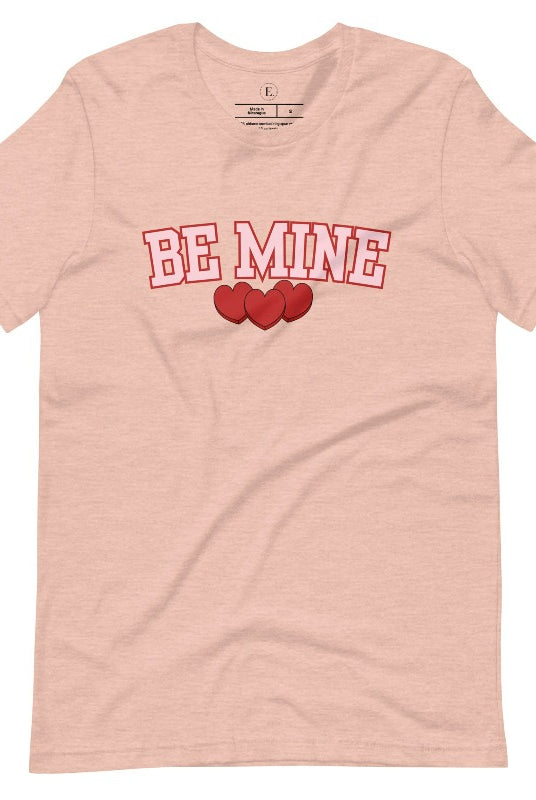 Elevate your Valentine's Day style with our "Be Mine" shirt! Featuring bold athletic lettering and three adorable hearts, on a heather prism peach shirt. 