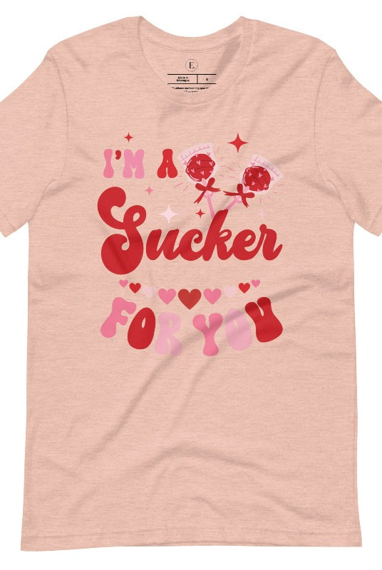 Indulge in the spirit of love with our Valentine's Day shirt! Adorned with charming Valentine lollipops and the playful saying, "I'm a sucker for you," on a heather prism peach shirt. 