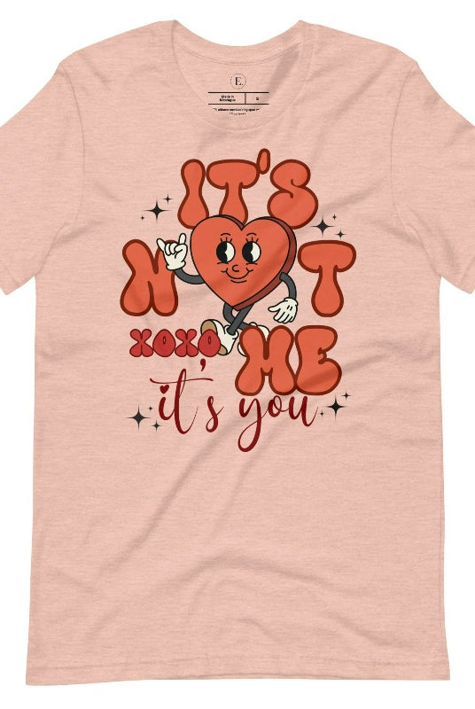 Celebrate Valentine's with our playful shirt! Featuring a bold heart and the message "It's not me, it's you," on a heather prism peach shirt. 