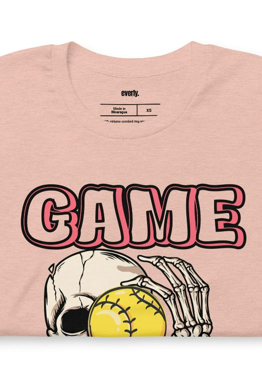 Softball game day skeleton skull holding a softball on a peach graphic tee.