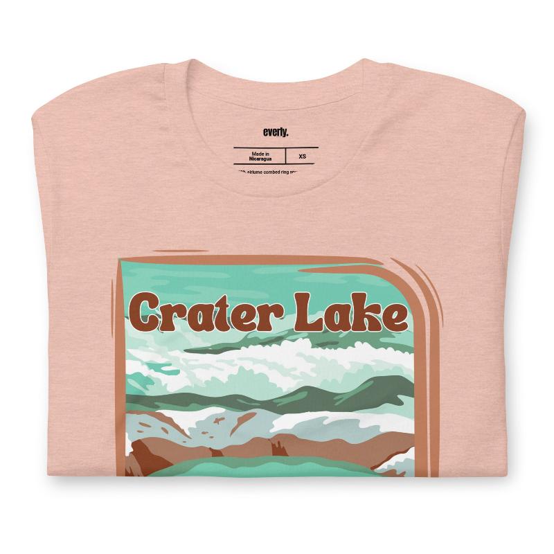 a colorful graphic of Crater Lake National Park, featuring mountains, water, and the text "Crater Lake National Park Oregon 1902 on a peach shirt. 