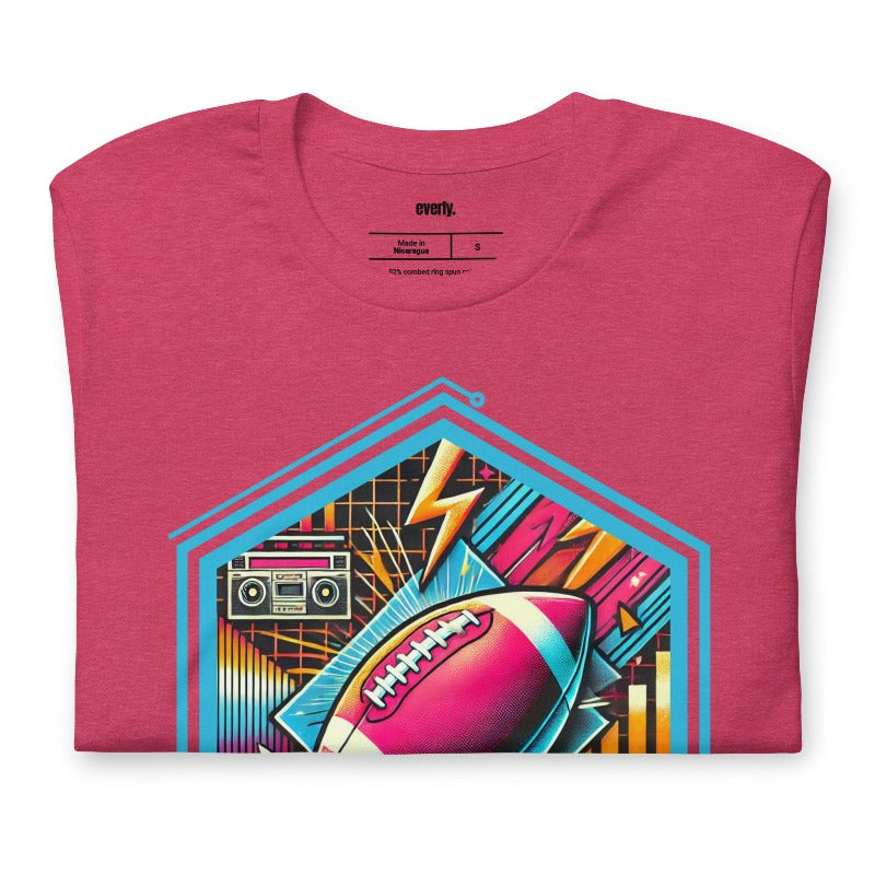 a vibrant neon design of a football with retro elements like boomboxes and geometric patterns, set in a hexagonal frame on a raspberry pink shirt.