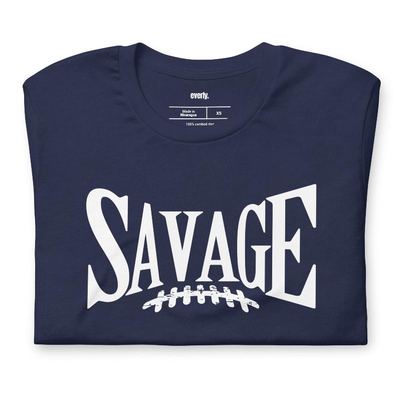 "Savage" in large, bold white letters with a football graphic underneath. The shirt is from Bella + Canvas and is made of 100% combed and ring-spun cotton on a navy shirt