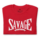 "Savage" in large, bold white letters with a football graphic underneath. The shirt is from Bella + Canvas and is made of 100% combed and ring-spun cotton on a red shirt