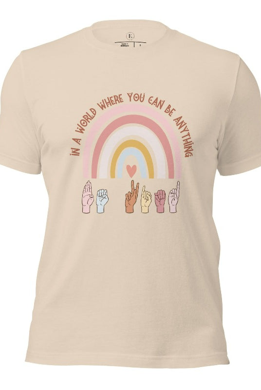 American sign language shirt with a rainbow and the phrase "In a world where you can be anything" and hands signing 'Be Kind' at the bottom on the rainbow on a soft cream colored shirt.