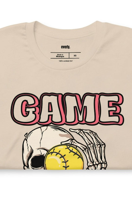 Softball game day skeleton skull holding a softball on a soft cream graphic tee.