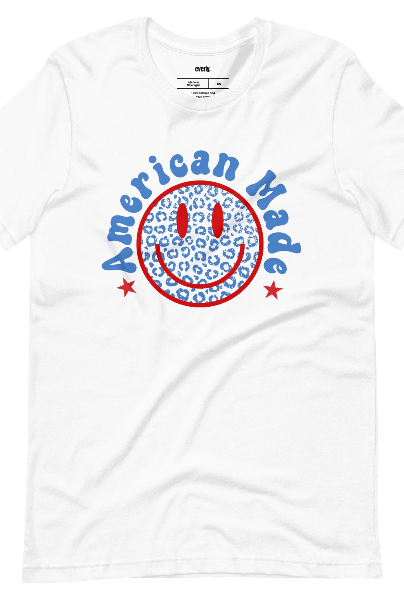 Close-up image of a USA July 4th graphic tee featuring the words 'American Made' surrounded by retro lettering around a bold blue cheetah print retro smiley face on the front. A playful and unique design perfect for celebrating July 4th in style on white graphic tee.