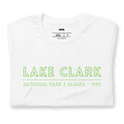 Back view of a black heather Bella + Canvas 3001 unisex shirt featuring a colorful design of Lake Clark National Park with mountains, lake, and wildlife. Inset shows the front view with "Lake Clark National Park | Alaska - 1980" text on a white shirt