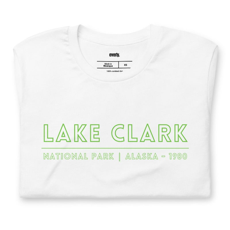 Back view of a black heather Bella + Canvas 3001 unisex shirt featuring a colorful design of Lake Clark National Park with mountains, lake, and wildlife. Inset shows the front view with "Lake Clark National Park | Alaska - 1980" text on a white shirt