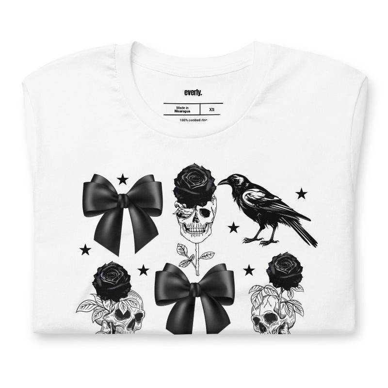 A white unisex t-shirt featuring a Halloween-themed design with black roses, skulls, ravens, bows, and stars. The design is printed in black and white, giving it a gothic and spooky vibe.