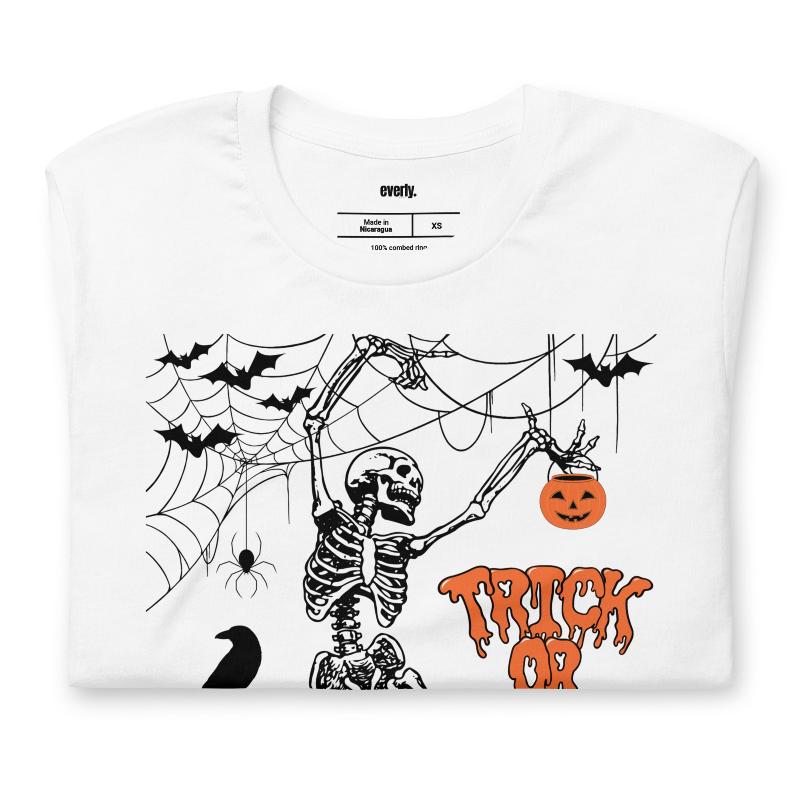 White t-shirt with a fun Halloween design featuring a skeleton, pumpkins, bats, and "Trick or Treat" text in a festive orange and black theme.