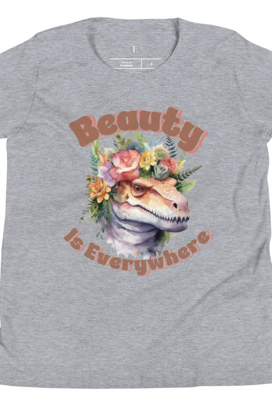 Unleash your child's wild side with our enchanting kids' shirt. Featuring a majestic dinosaur raptor adorned with a crown of flowers, this tee celebrates the beauty that surrounds us. With the inspiring message 'Beauty is Everywhere,' on an athletic heather grey shirt. 