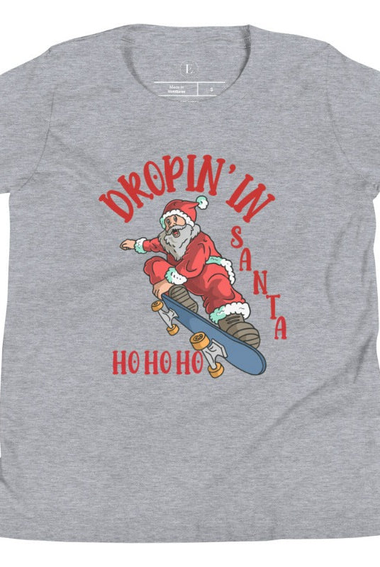 Get your kids in the holiday spirit with our unique, playful tee featuring Santa shredding on a skateboard with the phrase "Dropin' In Santa Ho Ho Ho." On an athletic heather grey shirt. 