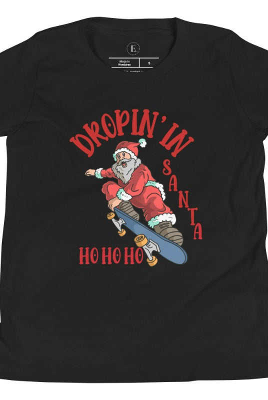Get your kids in the holiday spirit with our unique, playful tee featuring Santa shredding on a skateboard with the phrase "Dropin' In Santa Ho Ho Ho." On a black shirt. 