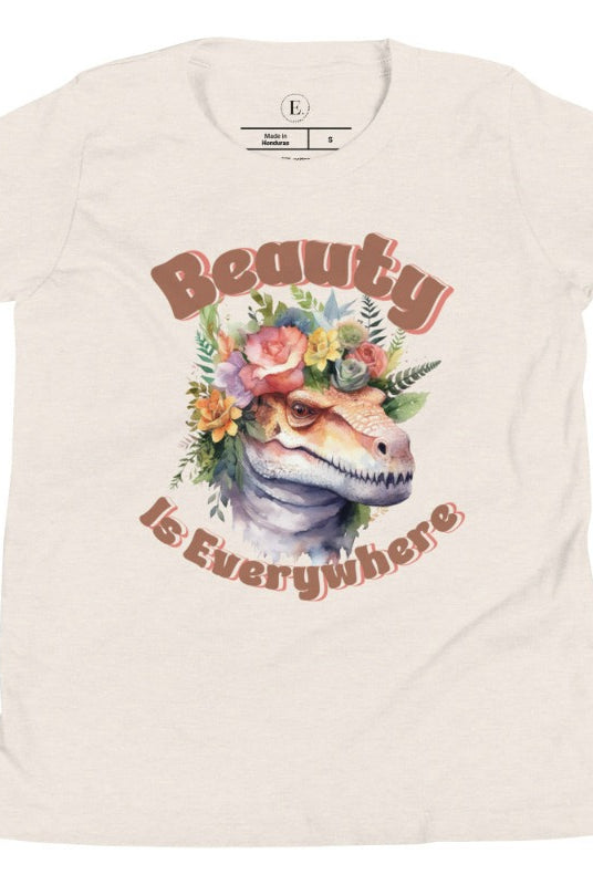 Unleash your child's wild side with our enchanting kids' shirt. Featuring a majestic dinosaur raptor adorned with a crown of flowers, this tee celebrates the beauty that surrounds us. With the inspiring message 'Beauty is Everywhere,' on a heather dust shirt. 