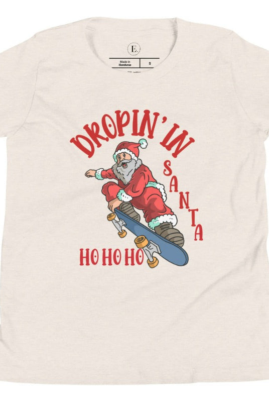 Get your kids in the holiday spirit with our unique, playful tee featuring Santa shredding on a skateboard with the phrase "Dropin' In Santa Ho Ho Ho." On a heather dust colored shirt. 