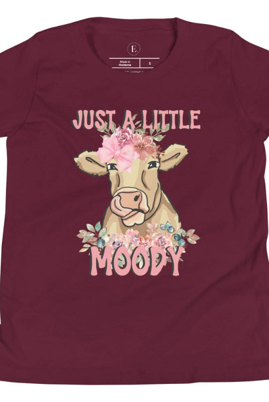 Our kid's shirt features an adorable highland cow with flowers and the quote 'Just a Little Moody,' adding humor and personality to the design on a maroon shirt. 